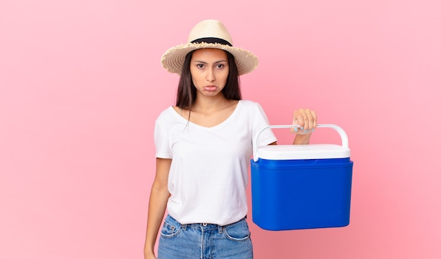 Bonita mujer hispana que se siente triste y llorona con una mirada infeliz y llorando y sosteniendo un refrigerador portátil