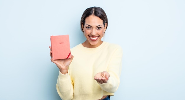 Bonita mujer hispana sonriendo alegremente con amabilidad y ofreciendo y mostrando un concepto. concepto de agenda