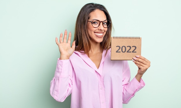 Bonita mujer hispana sonriendo alegremente, saludando con la mano, dándote la bienvenida y saludándote. concepto de calendario 2022