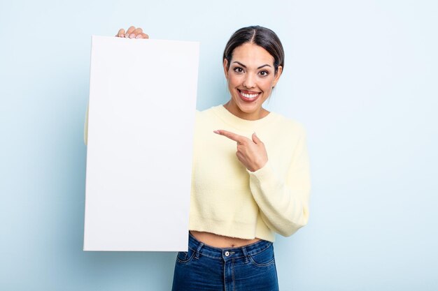 Bonita mujer hispana sonriendo alegremente, sintiéndose feliz y apuntando hacia un lado. concepto de espacio en blanco