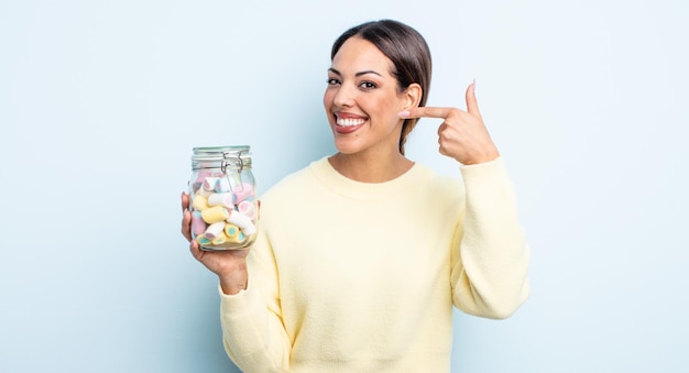 bonita mujer hispana sonriendo con confianza apuntando a su propia sonrisa amplia. concepto de caramelos de gelatina