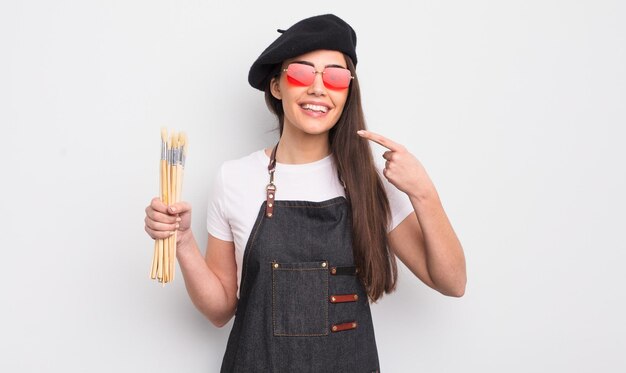 Bonita mujer hispana sonriendo con confianza apuntando a su propio concepto de artista de sonrisa amplia