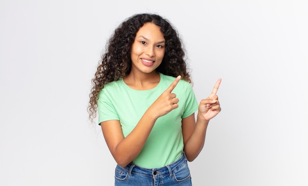 Foto bonita mujer hispana sonriendo felizmente y apuntando hacia un lado y hacia arriba con ambas manos mostrando el objeto en el espacio de la copia