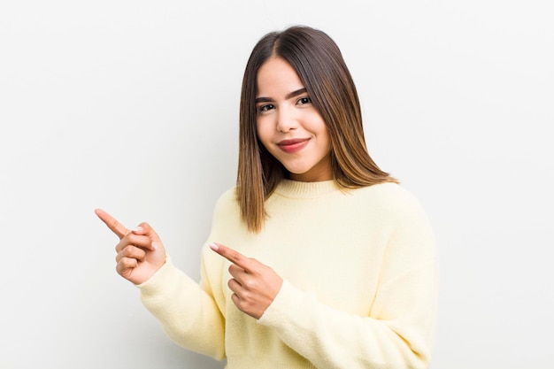 Bonita mujer hispana sonriendo felizmente y apuntando hacia un lado y hacia arriba con ambas manos mostrando el objeto en el espacio de la copia