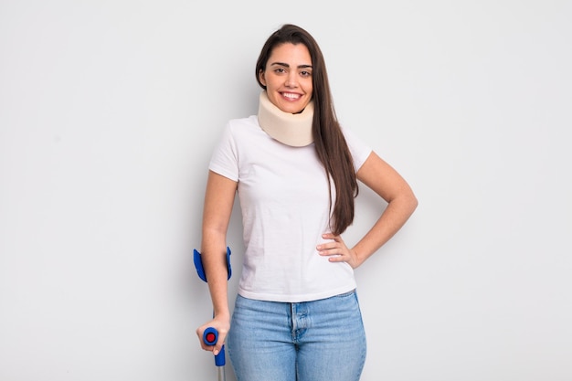 Bonita mujer hispana sonriendo felizmente con una mano en la cadera y un concepto seguro de accidente y lesión física