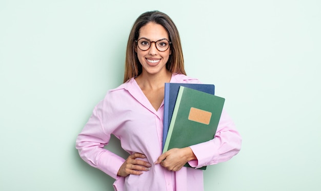 Bonita mujer hispana sonriendo felizmente con una mano en la cadera y confiada. concepto de cuadernos