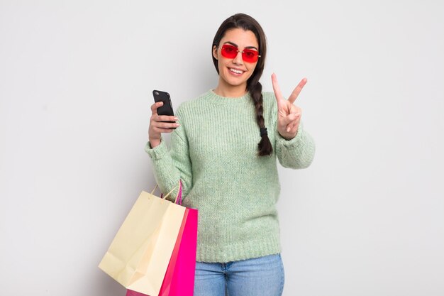 Bonita mujer hispana sonriendo y luciendo amigable mostrando las bolsas de compras número dos y el concepto de cliente