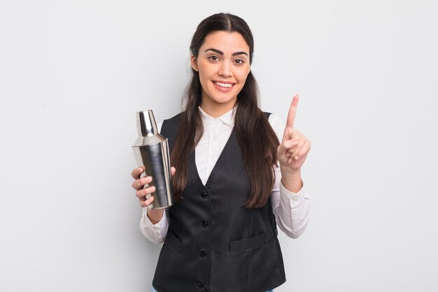 Bonita mujer hispana sonriendo y luciendo amigable, mostrando el número uno. concepto de cóctel barman