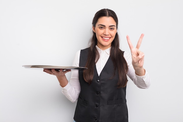 bonita mujer hispana sonriendo y luciendo feliz, gestando victoria o paz. camarero con concepto de bandeja