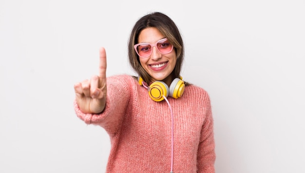 Bonita mujer hispana sonriendo con orgullo y confianza haciendo el concepto de auriculares número uno