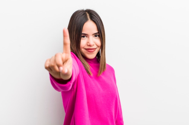 Bonita mujer hispana sonriendo con orgullo y confianza haciendo la pose número uno triunfalmente sintiéndose como una líder