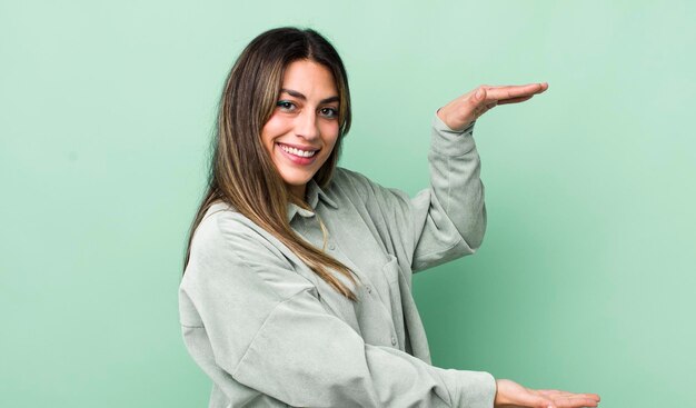 Bonita mujer hispana sonriendo sintiéndose feliz positiva y satisfecha sosteniendo o mostrando un objeto o concepto en el espacio de la copia