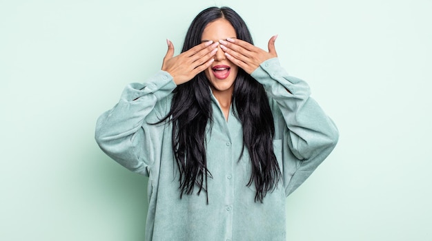 Bonita mujer hispana sonriendo y sintiéndose feliz, tapándose los ojos con ambas manos y esperando una sorpresa increíble