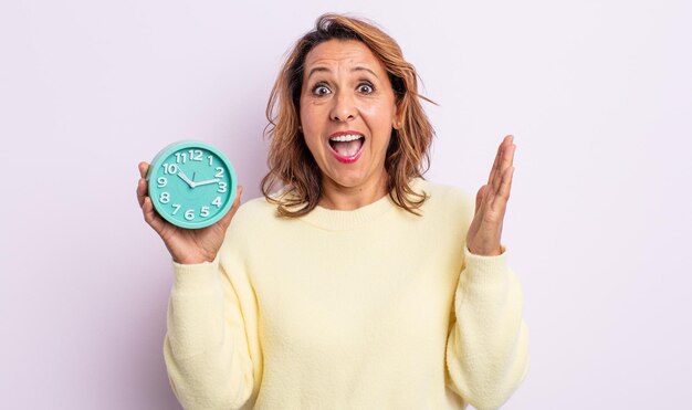 Bonita mujer de mediana edad que se siente feliz y asombrada por algo increíble. concepto de reloj despertador