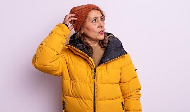 bonita mujer de mediana edad que se siente perpleja y confundida, rascándose la cabeza. concepto de invierno