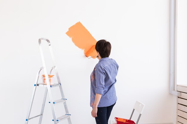 Bonita mujer de mediana edad con rodillo de pintura en el interior. Redecoración, renovación, reparación de apartamentos