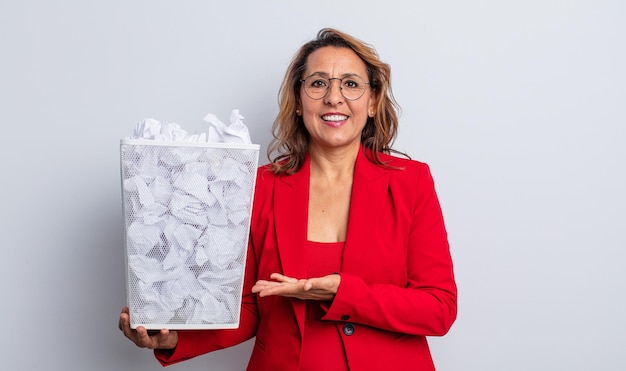 Bonita mujer de mediana edad sonriendo alegremente, sintiéndose feliz y mostrando un concepto. concepto de papelera de bolas de papel