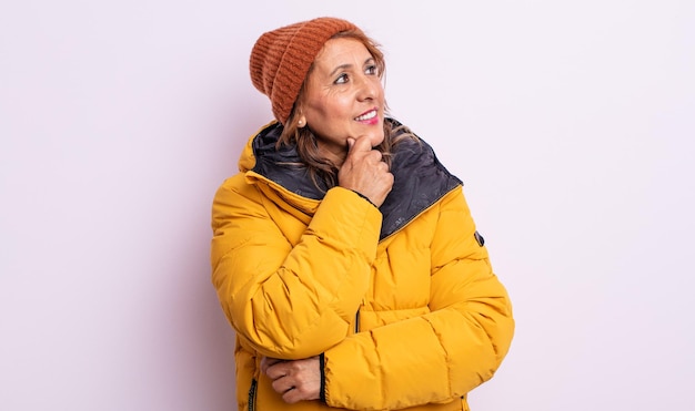 Bonita mujer de mediana edad sonriendo con una expresión feliz y segura con la mano en la barbilla. concepto de invierno