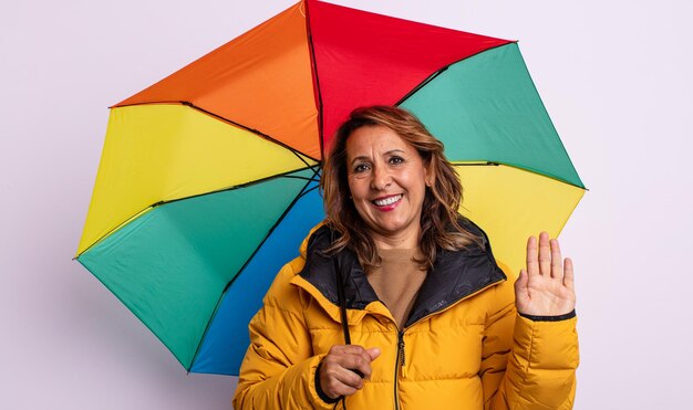 Bonita mujer de mediana edad sonriendo felizmente, saludando con la mano, dándote la bienvenida y saludándote. concepto de paraguas