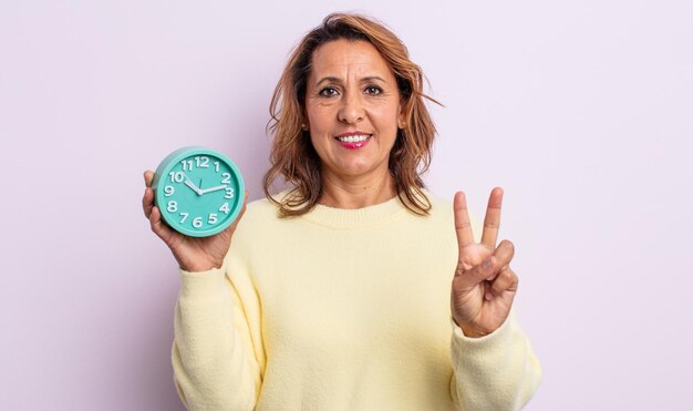 Foto bonita mujer de mediana edad sonriendo y luciendo amistosa, mostrando el número dos. concepto de despertador