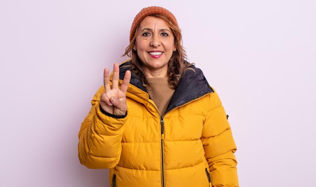 Bonita mujer de mediana edad sonriendo y luciendo amistosa, mostrando el número tres. concepto de invierno