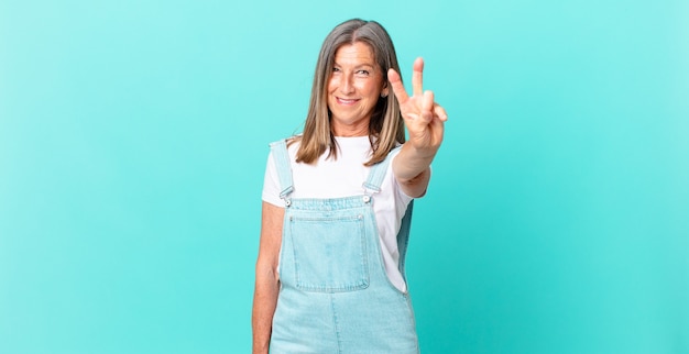 Bonita mujer de mediana edad sonriendo y mirando amistosamente, mostrando el número dos