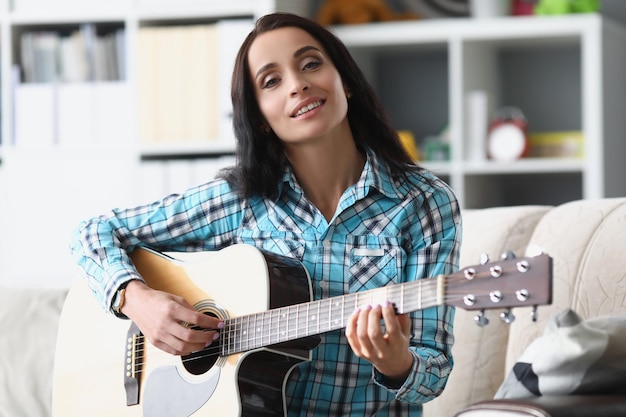 Bonita mujer morena tocando la guitarra en la sala de estar, la mujer pasa tiempo libre para aprender un nuevo pasatiempo