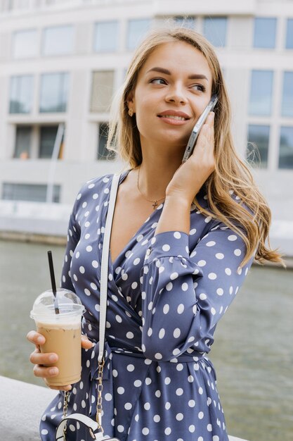 Una bonita mujer de negocios está hablando por teléfono con un cóctel de verano en las manos en el contexto de un paisaje urbano