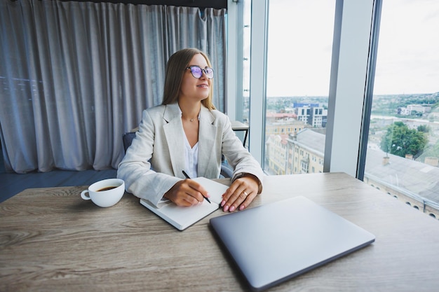 Bonita mujer de negocios mirando a través de un cuaderno centrado en el trabajo freelance trabajo remoto estudiando estudiar oficina moderna distanciamiento social interior Mujer en la oficina con gafas y computadora portátil