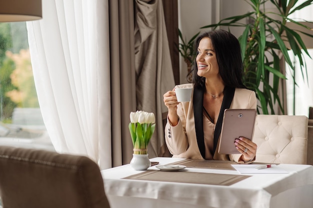 Bonita mujer de negocios usando una tableta para trabajar durante la pausa para el café en la cafetería