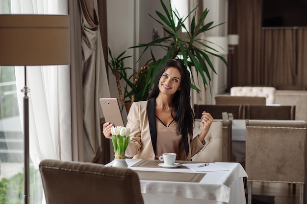 Bonita mujer de negocios usando una tableta para trabajar durante la pausa para el café en la cafetería