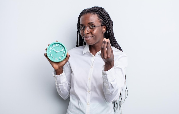 Bonita mujer negra haciendo gesto de capice o dinero, diciéndole que pague. concepto de reloj despertador