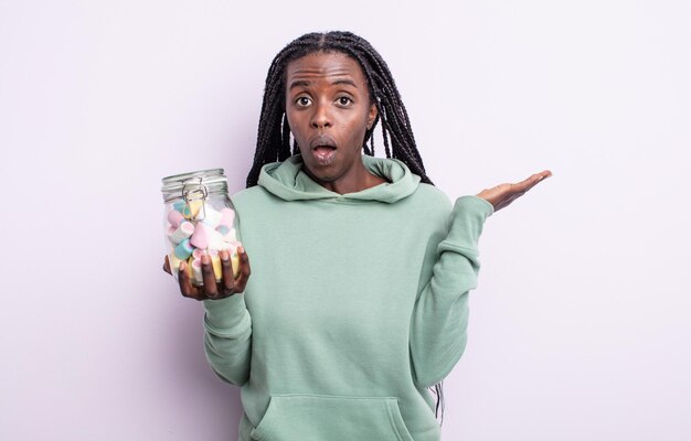 Bonita mujer negra que parece sorprendida y consternada, con la mandíbula caída sosteniendo un objeto. concepto de caramelos de gelatina