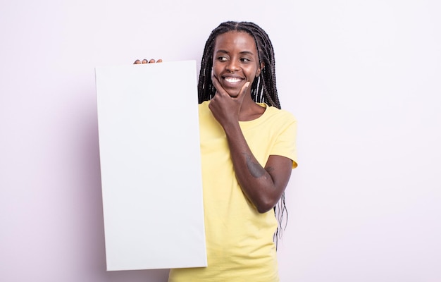 Bonita mujer negra sonriendo con una expresión feliz y segura con la mano en la barbilla. concepto de lienzo en blanco