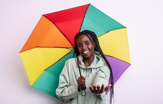 Bonita mujer negra sonriendo felizmente con amigable y ofreciendo y mostrando un concepto. concepto de paraguas