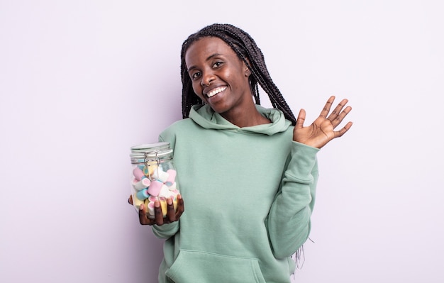 Bonita mujer negra sonriendo felizmente, saludando con la mano, dándote la bienvenida y saludándote. concepto de caramelos de gelatina