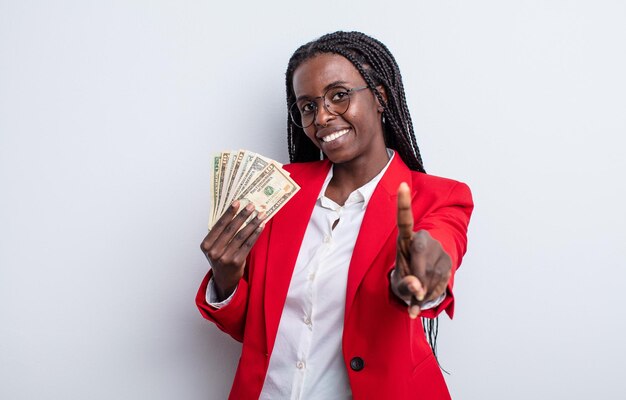 Bonita mujer negra sonriendo y mirando amigable, mostrando el número uno. concepto de billetes de dólar