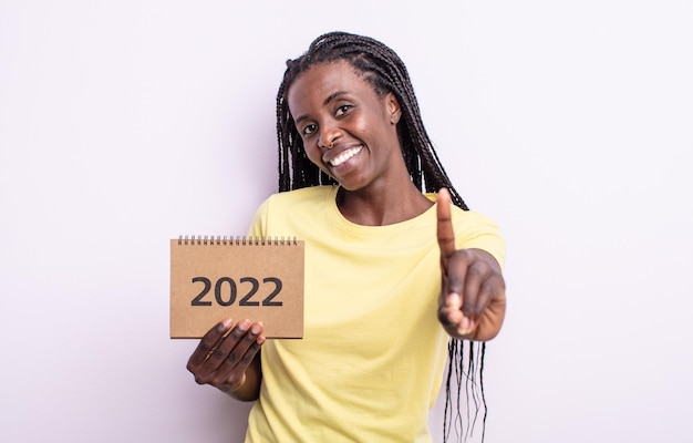 Bonita mujer negra sonriendo y mirando amigable, mostrando el número uno. Concepto de calendario 2022