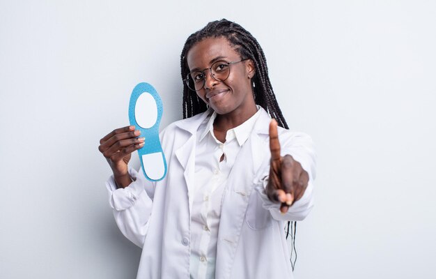 Bonita mujer negra sonriendo y mirando amigable, mostrando el número uno. concepto de podólogo