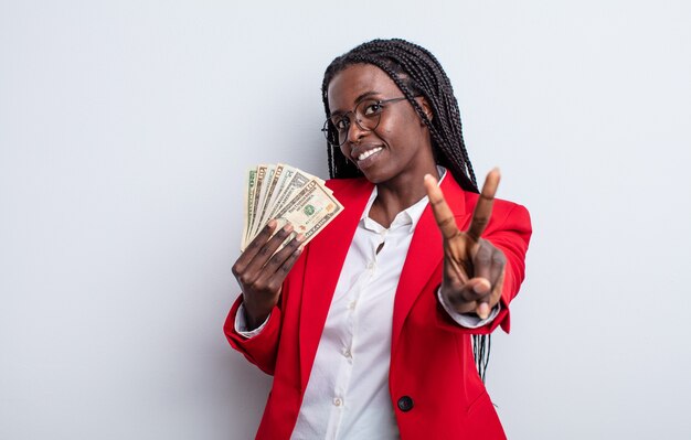 Bonita mujer negra sonriendo y mirando amigable, mostrando el número dos. concepto de billetes de dólar