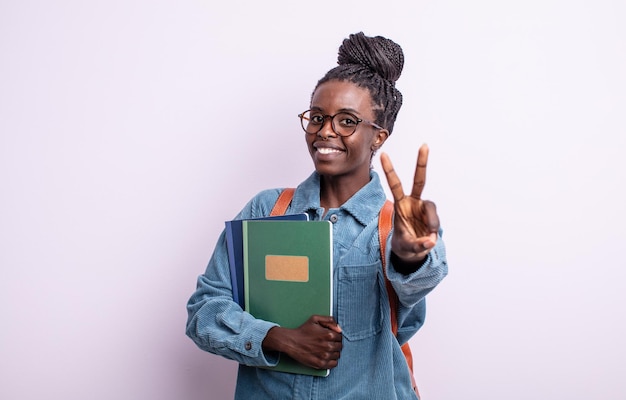 Bonita mujer negra sonriendo y mirando amigable, mostrando el número dos. estudiante con concepto de libros