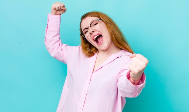 Bonita mujer pelirroja gritando triunfalmente luciendo como emocionada feliz y sorprendida ganadora celebrando