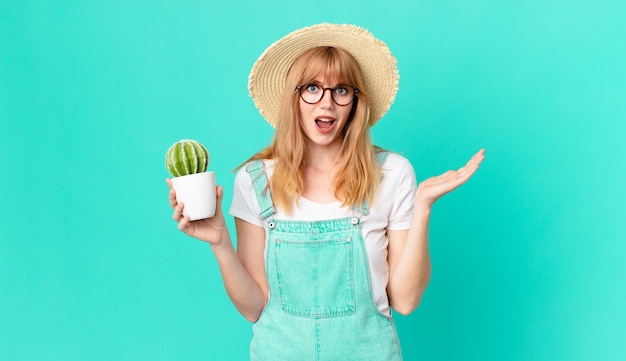 Bonita mujer pelirroja que se siente feliz y asombrada por algo increíble y sostiene un cactus en maceta. concepto de granjero