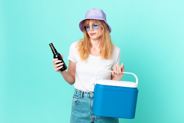 Bonita mujer pelirroja con un refrigerador portátil y una cerveza