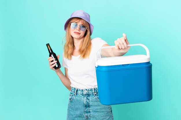 Bonita mujer pelirroja con un refrigerador portátil y una cerveza.