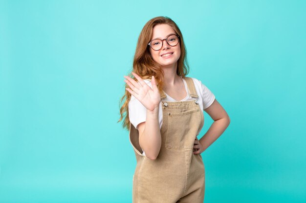 Bonita mujer pelirroja sonriendo alegremente, saludando con la mano, dándote la bienvenida y saludándote