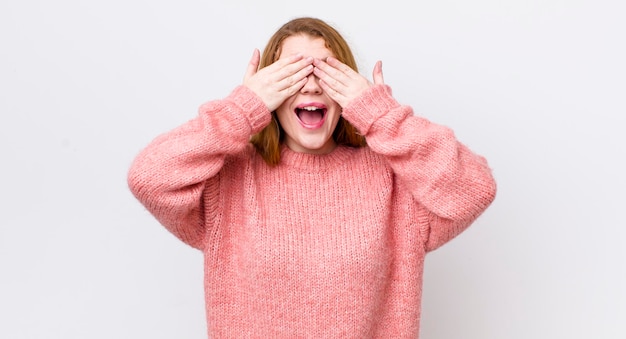 Bonita mujer pelirroja sonriendo y sintiéndose feliz cubriendo los ojos con ambas manos y esperando una sorpresa increíble