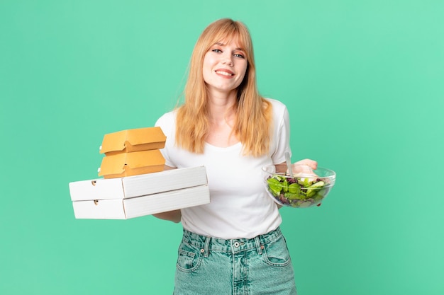 Bonita mujer pelirroja sosteniendo cajas de comida rápida y una ensalada