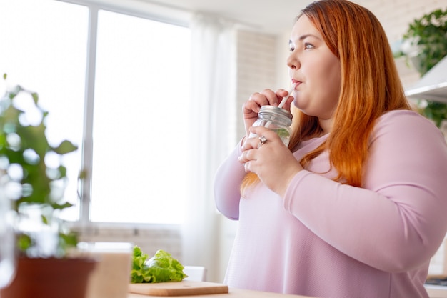 Bonita mujer pensativa sosteniendo una pajita mientras bebe su batido