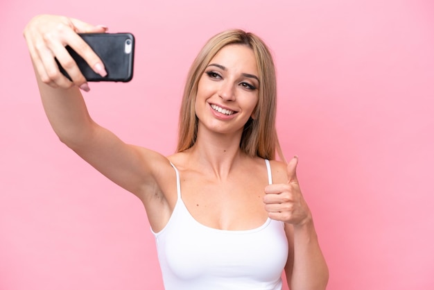 Foto bonita mujer rubia aislada de fondo rosa haciendo un selfie con teléfono móvil